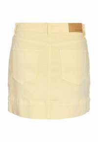 Mini-jupe en denim jaune clair avec deux poches arrière et un écusson en cuir marron sur la ceinture.