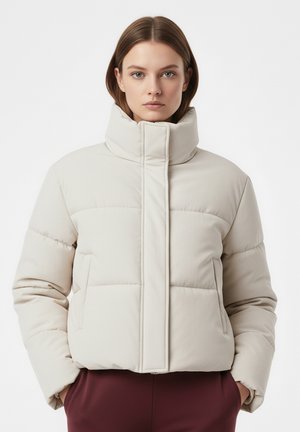 Beżowa pikowana kurtka z wysokim kołnierzem, prostokątnymi przeszyciami i bocznymi kieszeniami, wykonana z miękkiej tkaniny o gładkiej fakturze.