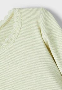 Lysegrønn ribbet langermet topp med bølget blondedetalj ved halsen. Stoffet er mykt med en subtil elastisitet.