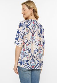 Blusa multicolore con un design a motivo blu, rosso e crema, maniche corte e orlo posteriore arrotondato. Tessuto morbido.