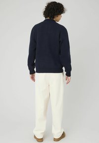 Pull en maille bleu marine avec ourlet et poignets côtelés, associé à un pantalon crème. Design uni, coupe standard, texture douce. Vue arrière simple.