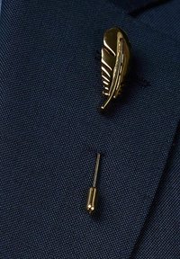 Guldfjädern på en lappnål placerad på en strukturerad marinblå tyg, med en smal guld baksidan nedan, som betonar den intrikata detaljer och finish.