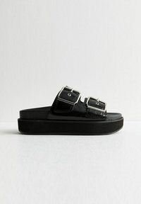 Černé platformové sandály s dvěma širokými přezkami, vyrobené z lesklého syntetického materiálu. Mají plochou podrážku a minimalistický design.