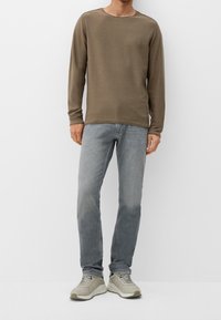 Camicia a maniche lunghe da uomo in taupe, realizzata in un materiale morbido. Abbinata a jeans grigi chiari e sneakers color crema con suole testurizzate.