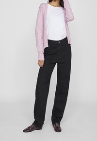 Schwarze weite Jeans kombiniert mit einem weißen T-Shirt und einem hellrosa Cardigan. Der Cardigan hat gerippte Bündchen und ein offenes Vorderdesign.