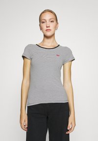 Tricou cu mânecă scurtă, dungat în alb și negru, cu guler rotund și o mică patch cu logo roșu în partea stângă.