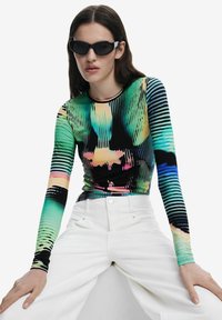 Bluză cu mânecă lungă, cu un model abstract multicolor, bază neagră și design ajustat. Asortată cu pantaloni albi cu talie înaltă și ochelari de soare negri eleganți.