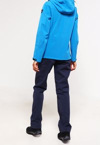 Blauwe waterdichte jas met een capuchon, gecombineerd met marineblauwe broek. De jas heeft een gladde textuur, terwijl de broek iets baggy is. Zwarte schoenen zichtbaar.