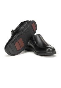 Zapatos negros de piel sin cordones con acabado texturizado, punta redonda y suelas de goma que presentan detalles rojos en el talón para mayor tracción.
