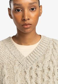 Light gray knitted sweater with a V-neck and textured cable pattern, layered over a cream-colored shirt. Smooth, soft fabric.