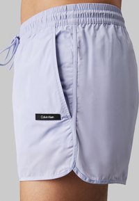 Lichtpaarse zwemshorts met elastische tailleband, verstelbaar trekkoord, zijzakken en een zwart Calvin Klein-logo op de zoom.