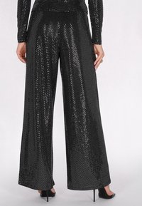 Zwarte wijde broek met een glanzend paillettenpatroon, voorzien van een soepel tailleband en subtiele textuur, gecombineerd met hoge hakken.