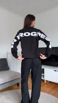 Sweat-shirt noir avec texte en style graffiti blanc "PROGRESS" sur le dos et la manche gauche. Le tissu semble lisse et décontracté.