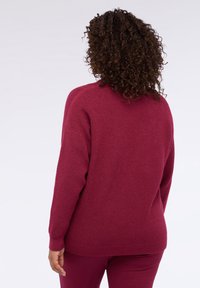 Maglione lavorato a maglia color granata con trama testurizzata, scollo rotondo e spalle scese. Presenta maniche lunghe e vestibilità comoda.