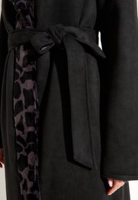 Zwarte robe gemaakt van zacht materiaal, met een ceintuur in de taille, en een contrasterende luipaardprint voering langs de voorkant.
