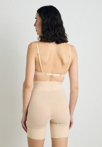 Gainage beige avec taille haute et longueur mi-cuisse, avec des bretelles réglables et une texture lisse, conçu pour un ajustement épuré.