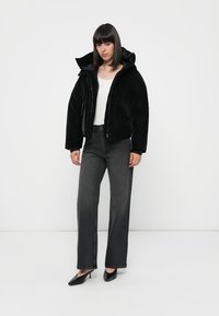 Giacca puffer nera con colletto alto e cappuccio, abbinata a jeans grigi a gamba larga e tacchi a punta neri. Tessuto dalla superficie liscia.
