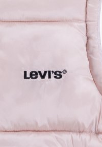 Light pink padded vest featuring a smooth, shiny texture with a black embroidered "Levi's" logo. Stitched detailing enhances the design.
