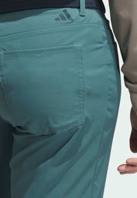 Türkise Hosen mit glatter Textur verfügen über eine Gesäßtasche und ein dezentes schwarzes Logo. Der Bund ist mit einem gewebten Detail verstellbar.