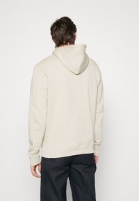 Sudadera de un tono beige claro con una costura central en la parte trasera, bolsillo tipo canguro y capucha con cuerda ajustable. Tejido suave con puños y dobladillo acanalados.