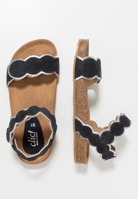 Černé semišové sandály se zvlněným vzorem a stříbrnými akcenty. Podešev je z korku s texturovaným protiskluzovým povrchem. Uzavřená špička, otevřená pata.