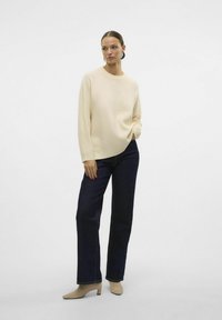 Cremefarvet, afslappet sweater med rund hals; sat sammen med mørkeblå, lige ben jeans og beige, mellemhøje sko.