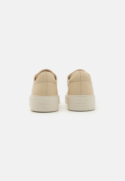 Beige lærersneakers med en glat overflade, præsenterende et minimalistisk design og en hvid gummisål. Mærkets label synlig på hælen.