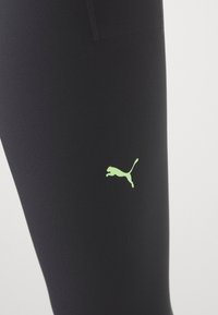 Czarne legginsy sportowe o gładkiej strukturze, z małym zielonym logo Pumy na dolnej części nogawki oraz dyskretną kieszonką na zamek.