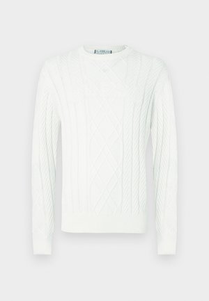 Valkoinen palmikkoneulepaita, jossa on pitkät hihat ja teksturoitu "GUESS"-logo rinnassa, sekä resorit hihansuissa ja helmassa.