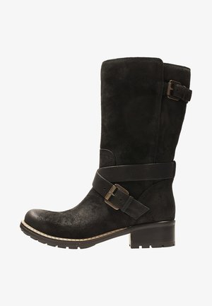 Zwarte suède kniehoge laars met een ronde neus, opvallende zijgesp en een dikke lage hak. Geaccentueerd met een contrasterende riemdetail.