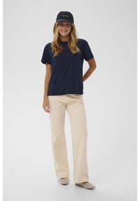 Mornarsko majico in svetlo bež široke hlače dopolnjuje mornarska kapa z zlatim besedilom. Obutev z teksturo in obliko z žebljički zaključuje videz.