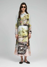 Robe longue à manches boutonnées arborant un imprimé tropical avec des palmiers, des voitures anciennes et des personnages. Fabriquée en tissu léger et brillant. Accents colorés.