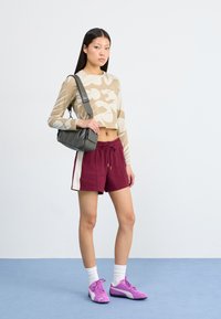 Top court beige avec un motif camouflage, shorts bordeaux avec des rayures sur les côtés, sac bandoulière gris et baskets violettes.