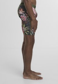 Czarne kwieciste krótkie spodenki kąpielowe z różowymi i zielonymi tropikalnymi wzorami, elastycznym pasem i dopasowanym krojem, pokazane z widoku bocznego.