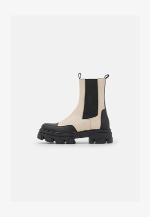 Robusna dvobojna bež i crna gležnjača s elastičnim bočnim panelima i čvrstim profiliranim potplatom na bijeloj pozadini.