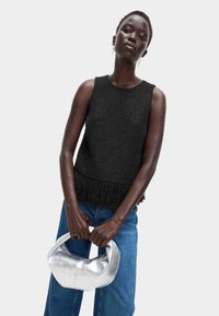 Top negro de punto sin mangas con un acabado texturizado y detalle de flecos en el dobladillo, combinado con jeans de tiro alto azules y un bolso plateado.