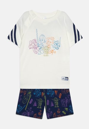 Maglietta a maniche corte color crema con stampa di personaggi blu e arancioni; pantaloni corti blu navy con motivi di personaggi dei cartoni animati colorati e accenti di logo.
