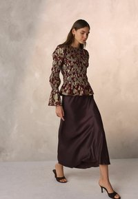 Burgundia värvi pika varrukaga peplum-top koos kuldse lillemustriga, kombineeritud tumeda satiinist midi-seeliku ja pruuni avatud toe kontsakingadega.