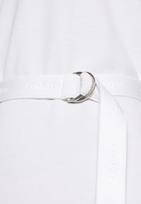 Biała odzież z teksturowanej tkaniny, ozdobiona wąskim białym paskiem i detalami ze srebrnego metalu, z napisem "Calvin Klein".