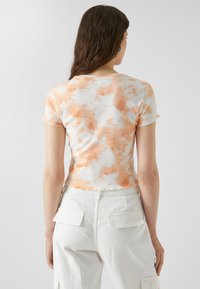 Korte mouwen cropped t-shirt in het wit met een oranje tie-dye patroon, voorzien van een ronde halslijn en zacht, textured stof.
