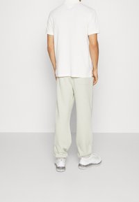 Polo bianco, pantaloni della tuta grigio chiaro con tasca sul retro e sneakers bianche con dettagli glitterati, viste da dietro.