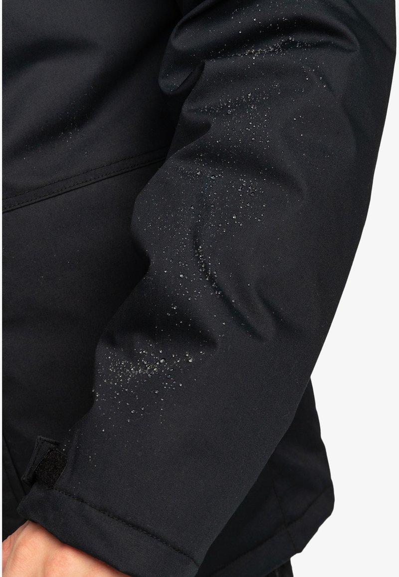 Manga de chaqueta impermeable negra con gotas de agua visibles y un ligero brillo. El material es suave, con una textura sutil y costuras reforzadas.