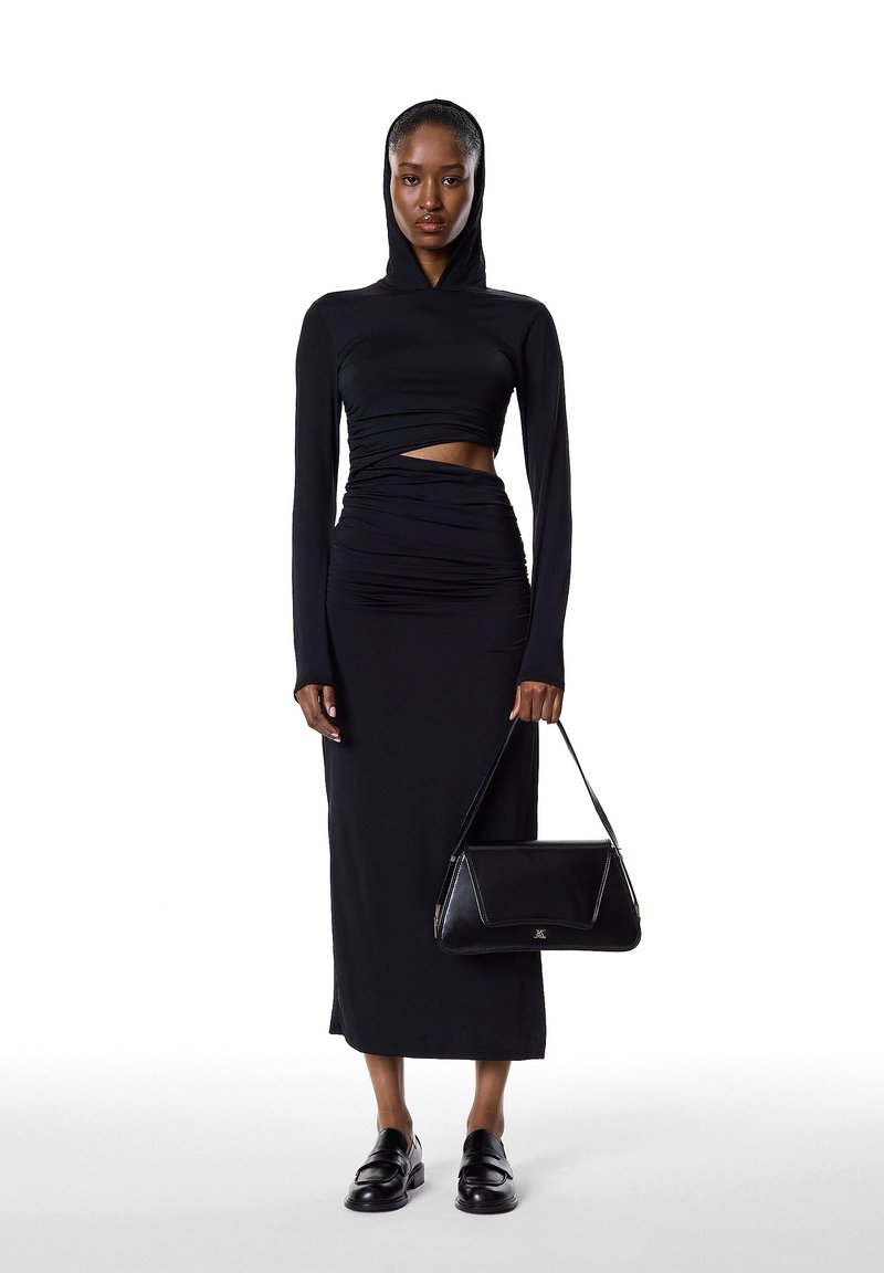 Vestido negro de manga larga con capucha, con detalles fruncidos y un corte en el abdomen. Combinado con un bolso estructurado negro y mocasines.