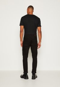 Svart kortärmad t-shirt, matchad med svarta tajta jeans, sedd bakifrån. Enkelt design, inga mönster, med uppvikta ärmar och svarta skor.