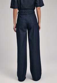 Pantaloni in denim di colore blu scuro, a gamba larga e vita alta, con tasche posteriori e dettagli di cucitura visibili. Tessuto liscio con una vestibilità strutturata.