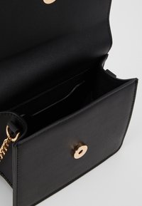 Borsa a tracolla in finta pelle nera con chiusura a scatto in tono oro. Presenta un interno aperto con una tasca a inserto e fodera testurizzata.