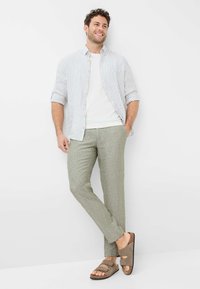 Lightweight, striped button-up shirt with rolled sleeves, white t-shirt, green linen pants, and brown sandals with dual straps.