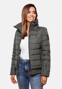 Giubbotto piumino grigio scuro con colletto alto, tasche con zip, design trapuntato e una toppa in pelle marrone con il logo sulla manica sinistra.