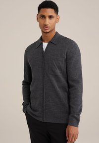 Dunkelgrauer Reißverschluss-Pullover aus strukturiertem Strickstoff, mit einem Kragen und einer einzelnen Brusttasche. Der Schnitt ist lässig.