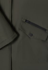 Kurtka w oliwkowej zieleni z gładką, matową fakturą tkaniny, kieszenią na piersi na zamek oraz kieszenią z patką na guziki na przednim rękawie.